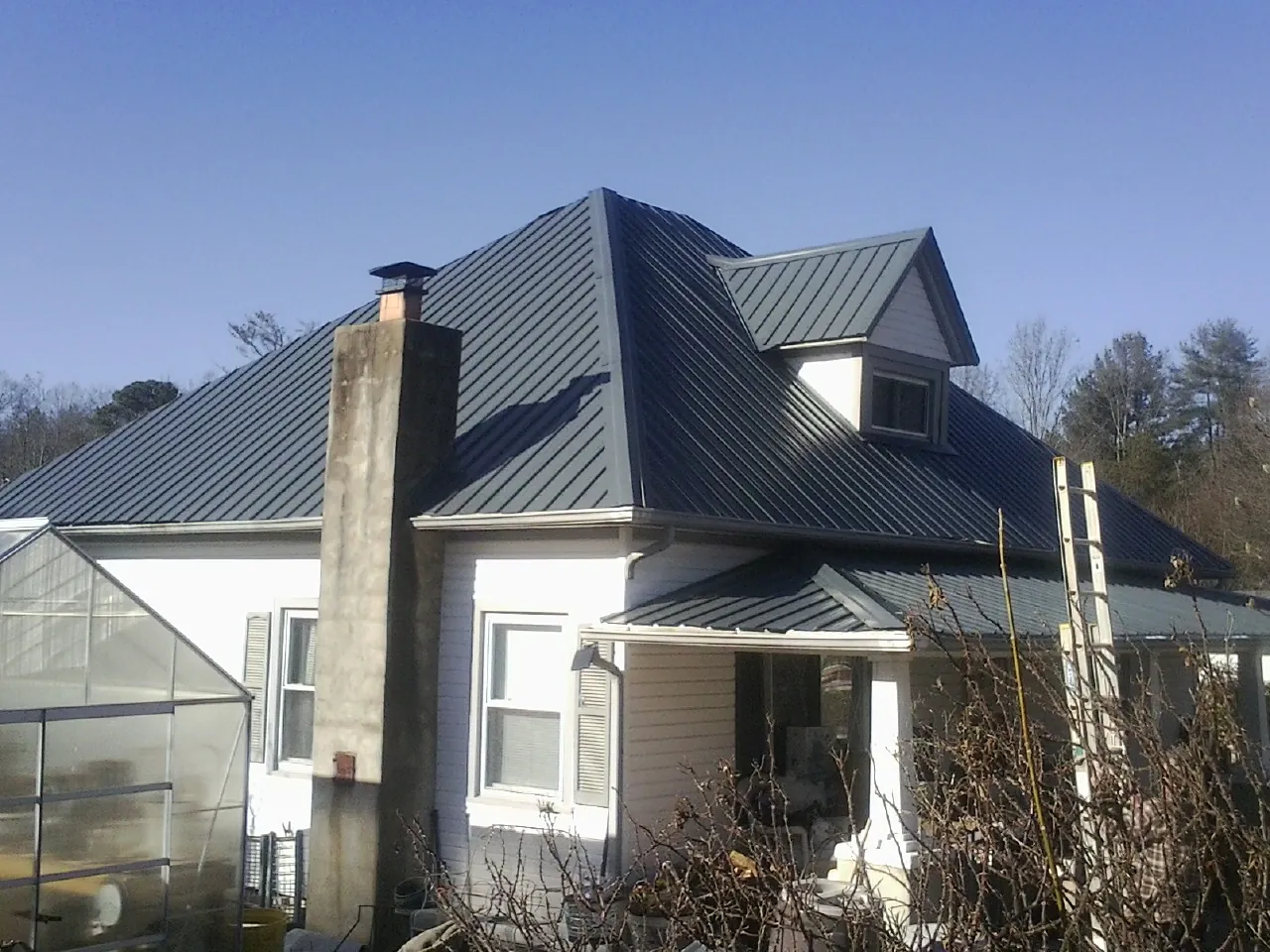 Dark blue standing seam metal roof on a white farmhouse with dormer — Slate & Tile Roof Repair by Roofing Brothers in Freeburg