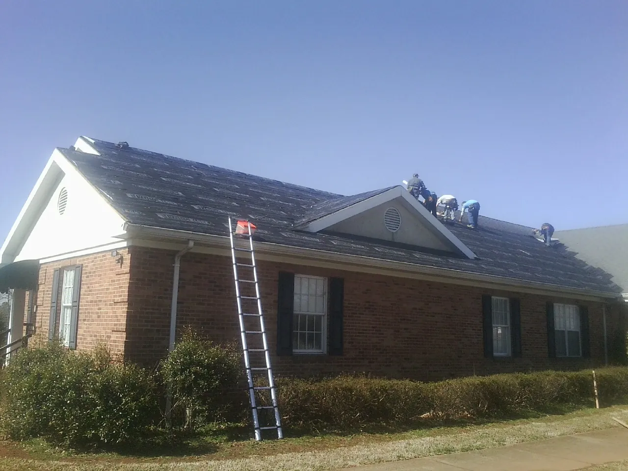 Crew tearing shingles off a brick ranch roof with a ladder set — Metal Roof Repair work by our crew in Freeburg