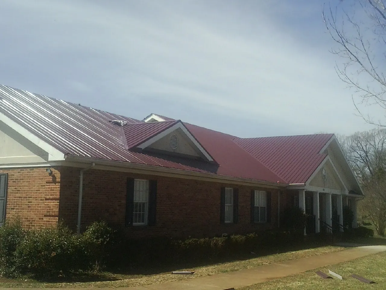 Red metal roof with gabled entries on a long brick building, from a Hail Damage Roof Repair job in Freeburg