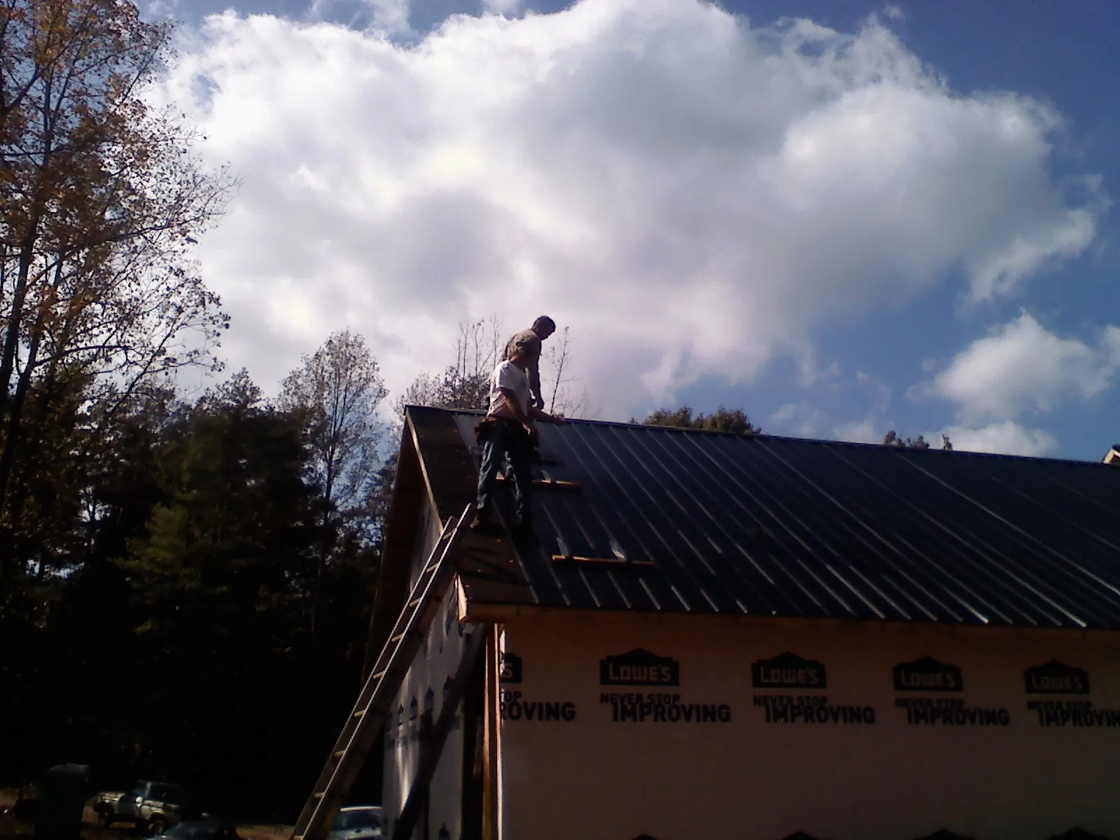 Roofer fastening dark metal panels high against a cloudy sky, from a Roof Inspection job in Freeburg