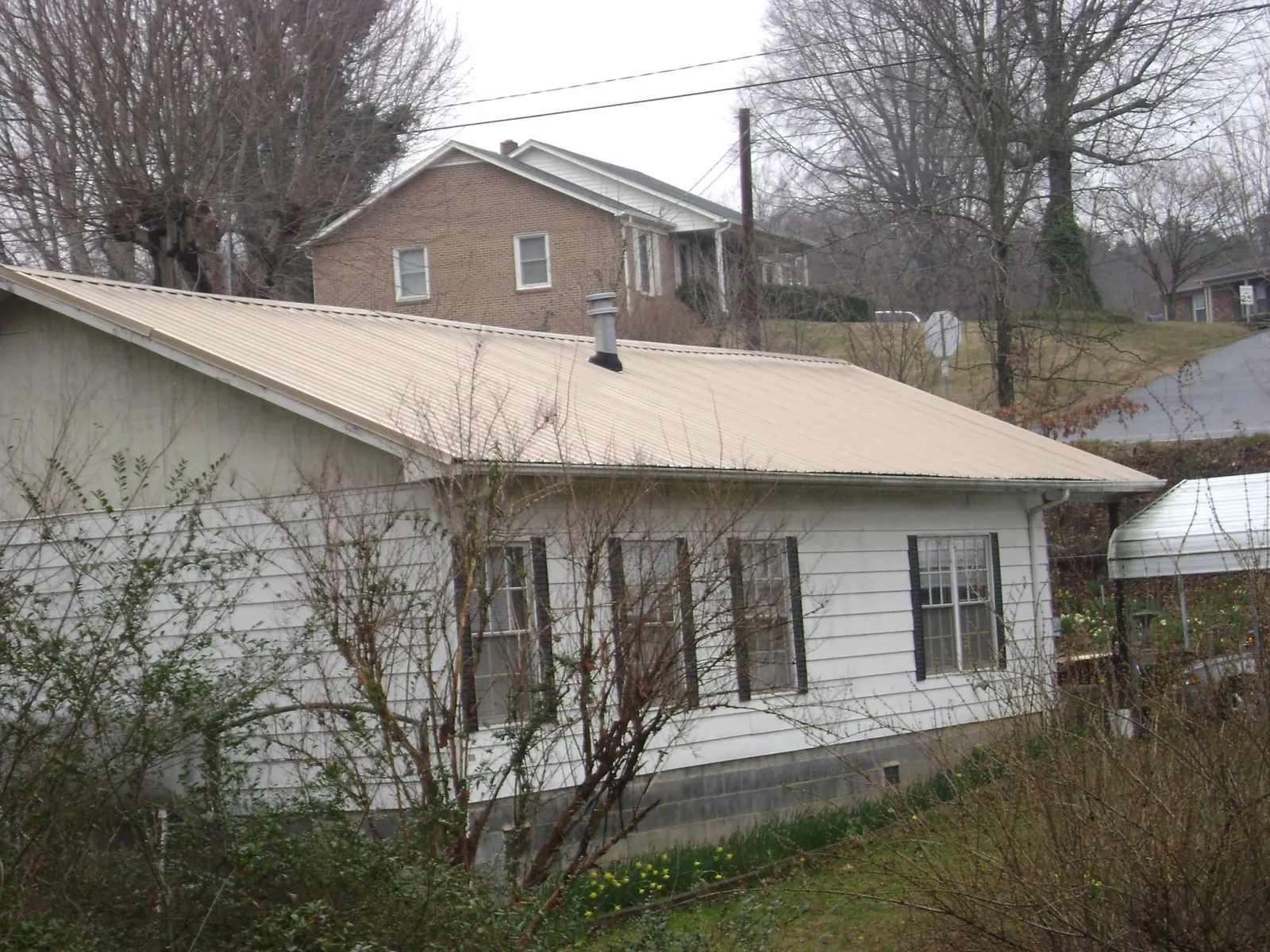 Tan metal roof on a white sided house set into a hillside — Commercial Roofing by Roofing Brothers in Freeburg